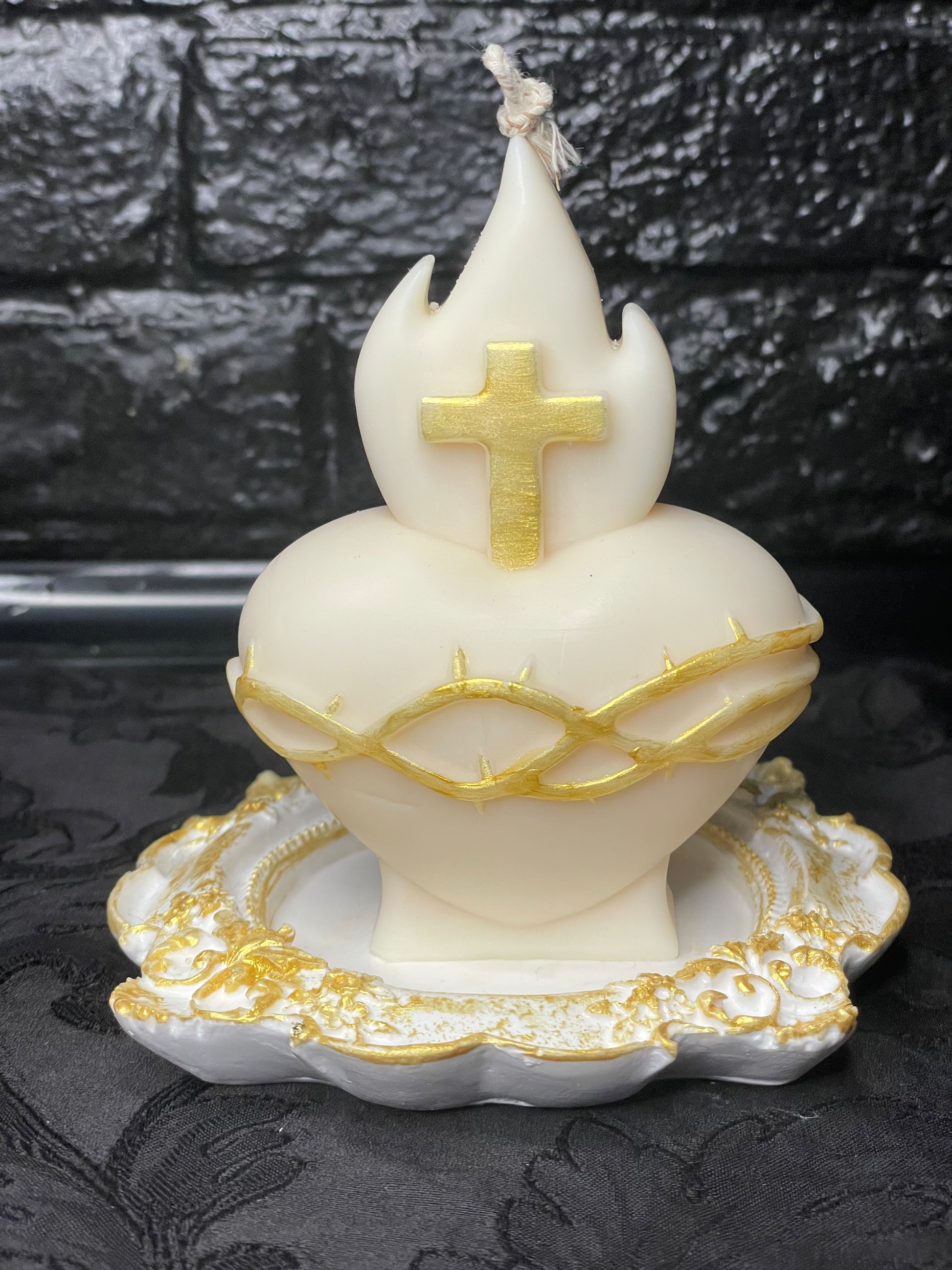 Bougie sculpturale Sacré-Cœur en cire de soja blanche avec détails dorés sur la croix et la couronne d'épines, posée sur un socle baroque blanc et or.